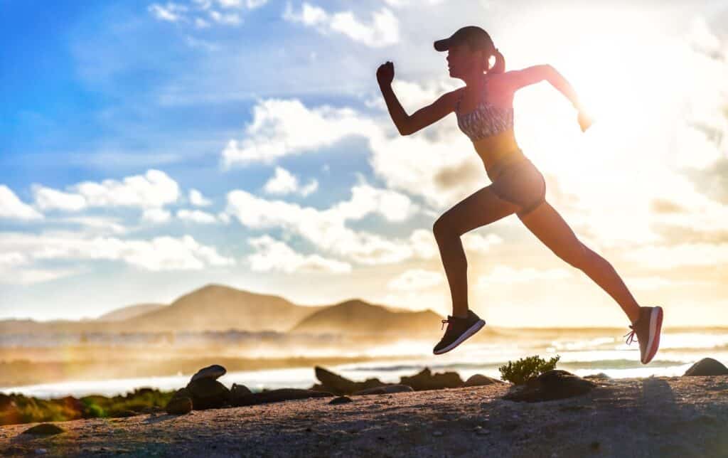 Una mujer corriendo en un sendero con montañas y nubes de fondo