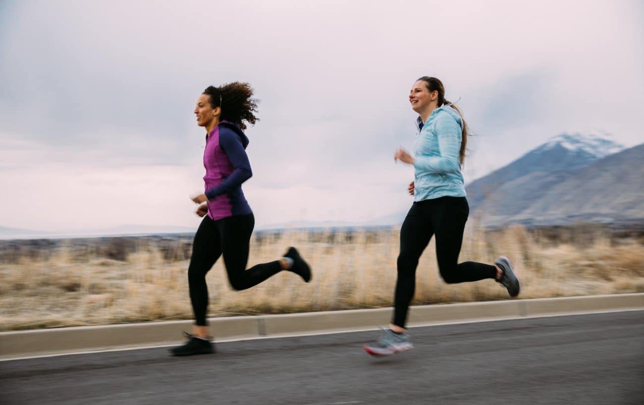 dos mujeres corriendo en una carretera con montañas detrás