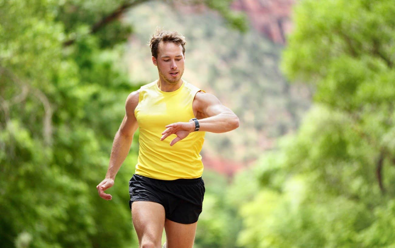 un hombre corriendo en la naturaleza revisando su reloj