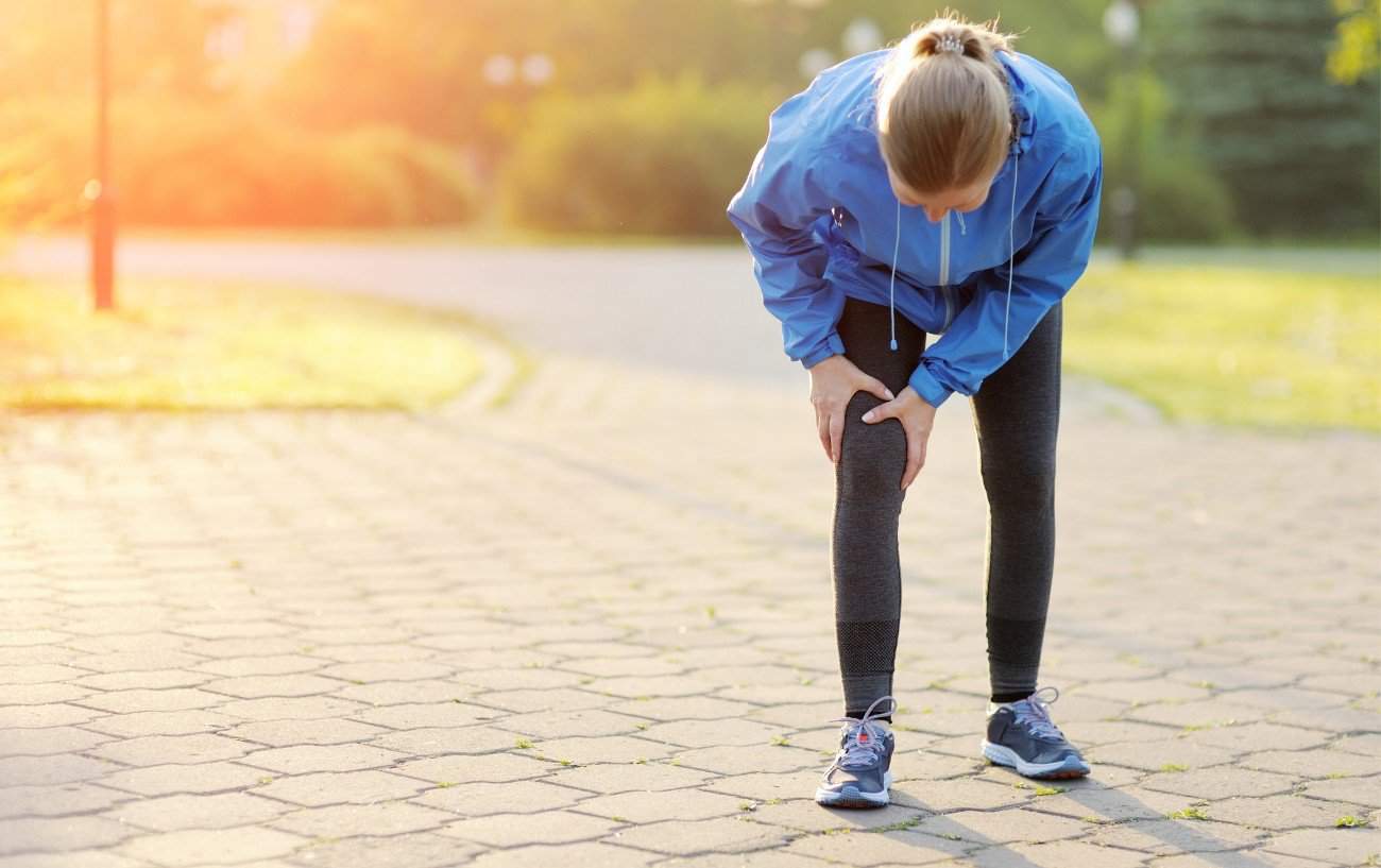 Una persona vestida de azul sosteniendo su rodilla mientras corre.