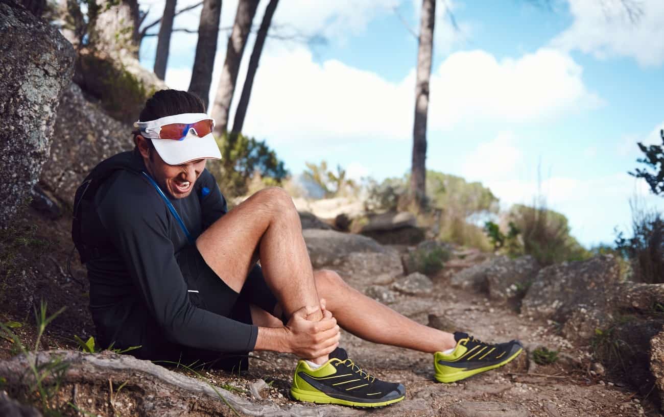 Un corredor sentado en un sendero rocoso sosteniendo su tobillo.