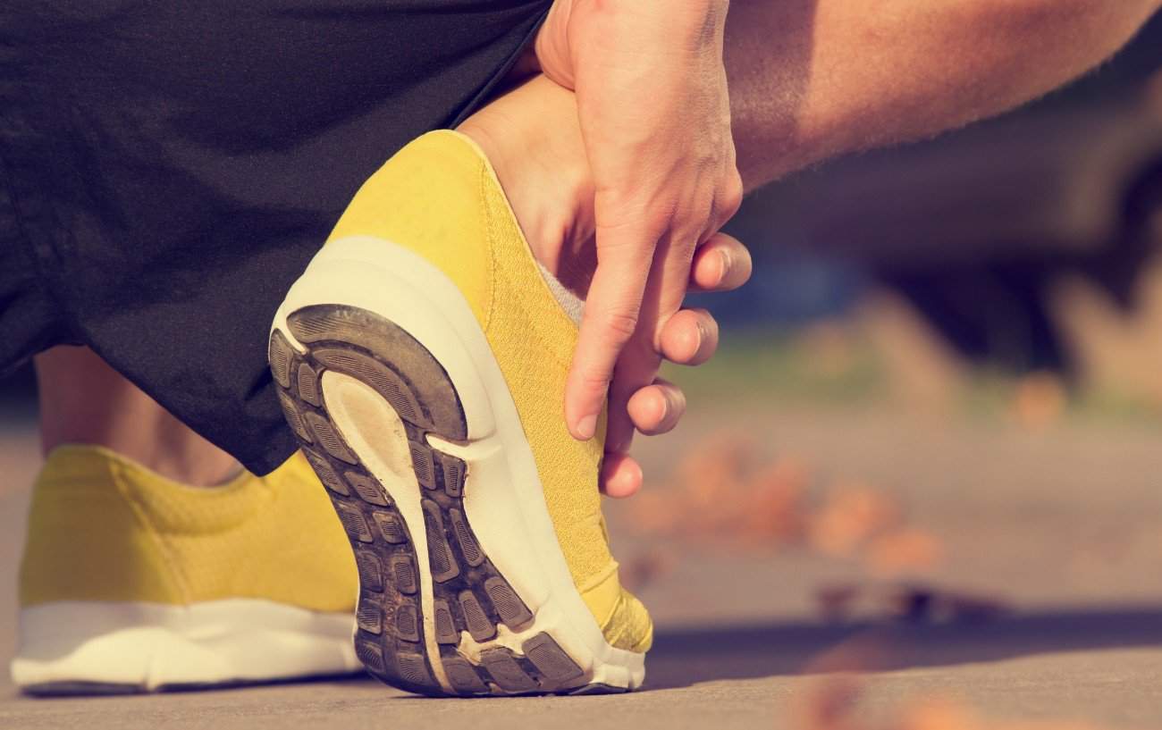 Una persona con zapatos para correr amarillos sostiene su tobillo.