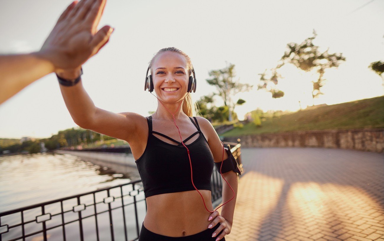 a hand from behind the camera hi-fiving a female runner wearing headphones