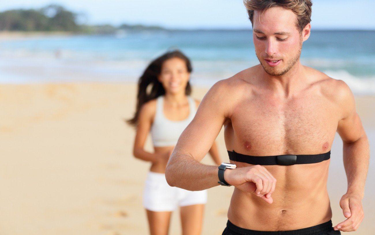 Personas corriendo en la playa con un monitor de frecuencia cardíaca.