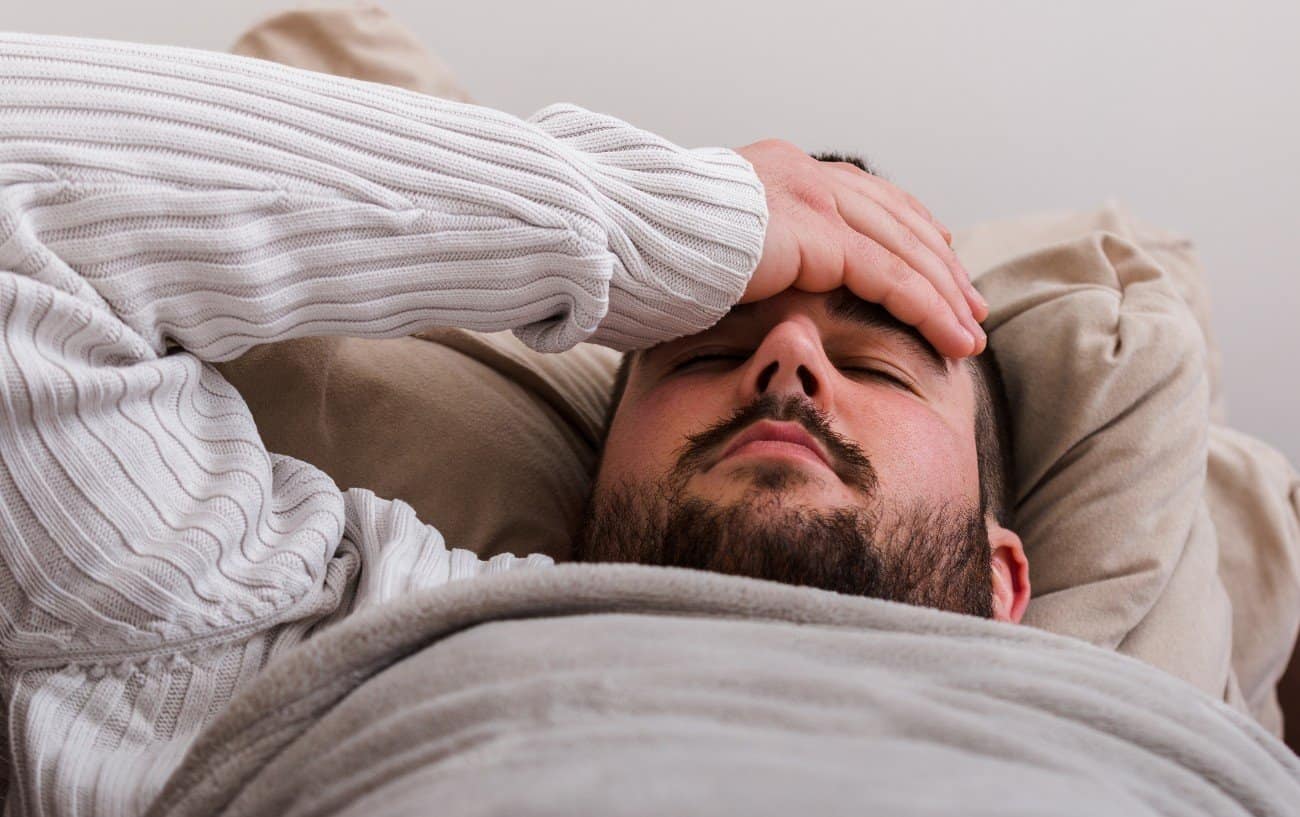 A man lying down holding his forehead.