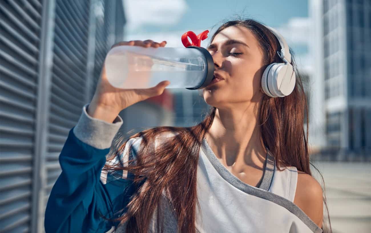 Una mujer bebiendo agua después de hacer ejercicio.