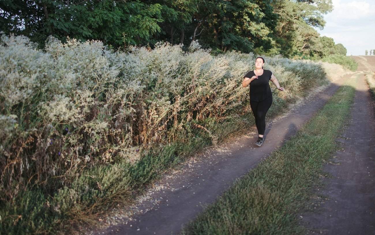 Una mujer aprendiendo cómo empezar a correr cuando tienes sobrepeso en un sendero.