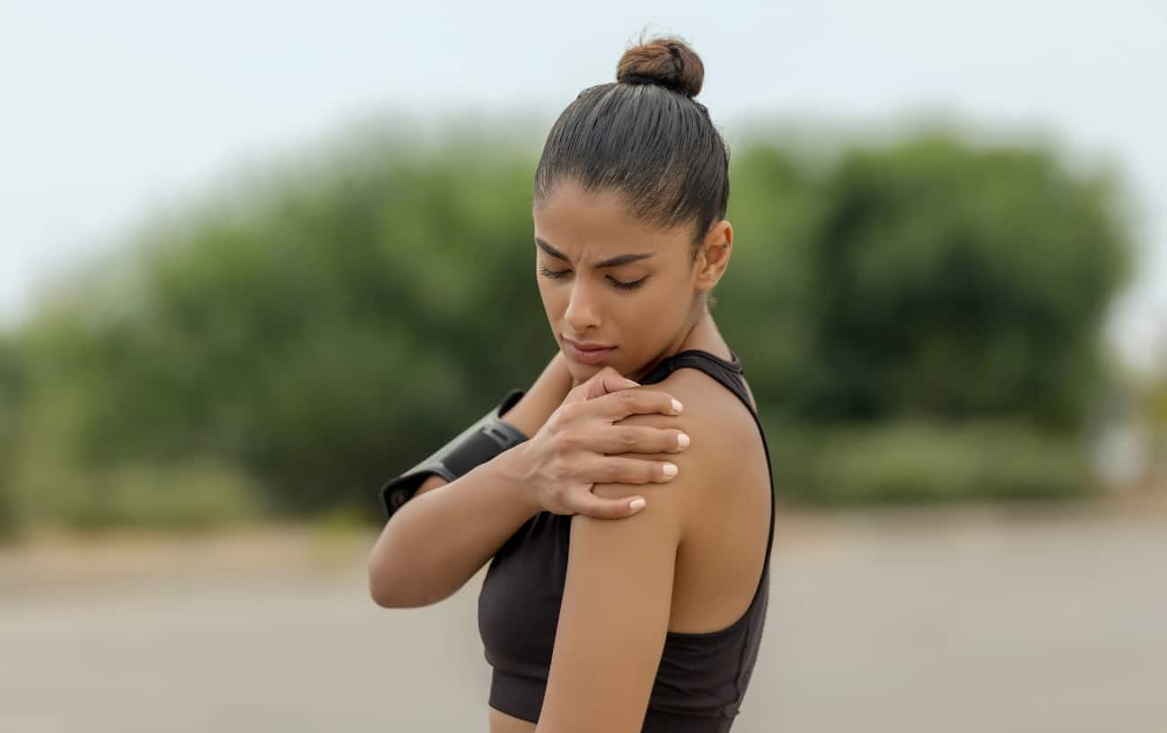 Una mujer experimentando dolor de hombros al correr.