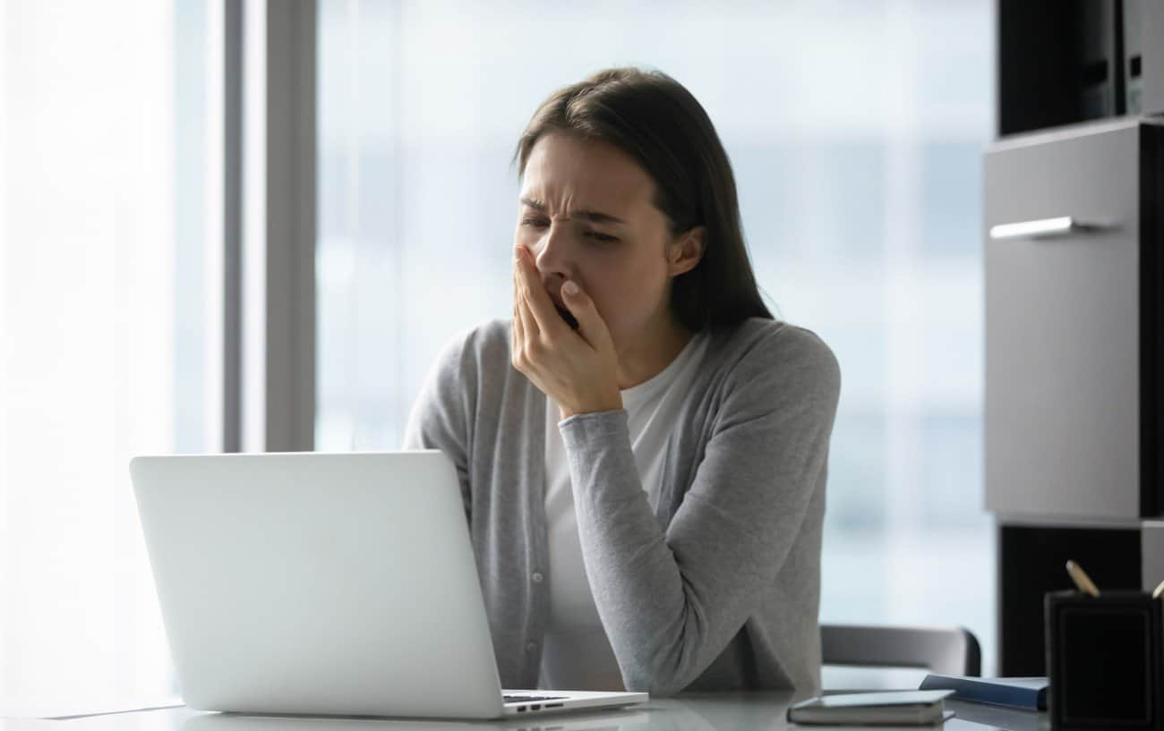 Una persona en su computadora bostezando, sintiéndose cansada después de comer.