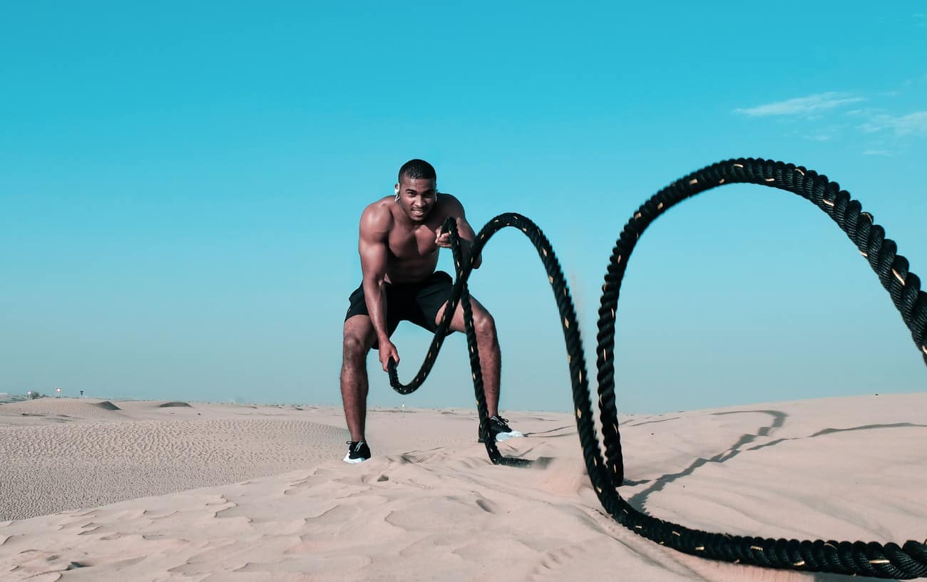 A man on the beach doing battlerope.