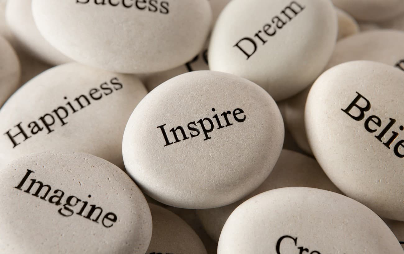 A pile of rocks that have words engraved on them such as inspire, believe, dream, happiness, and imagine.