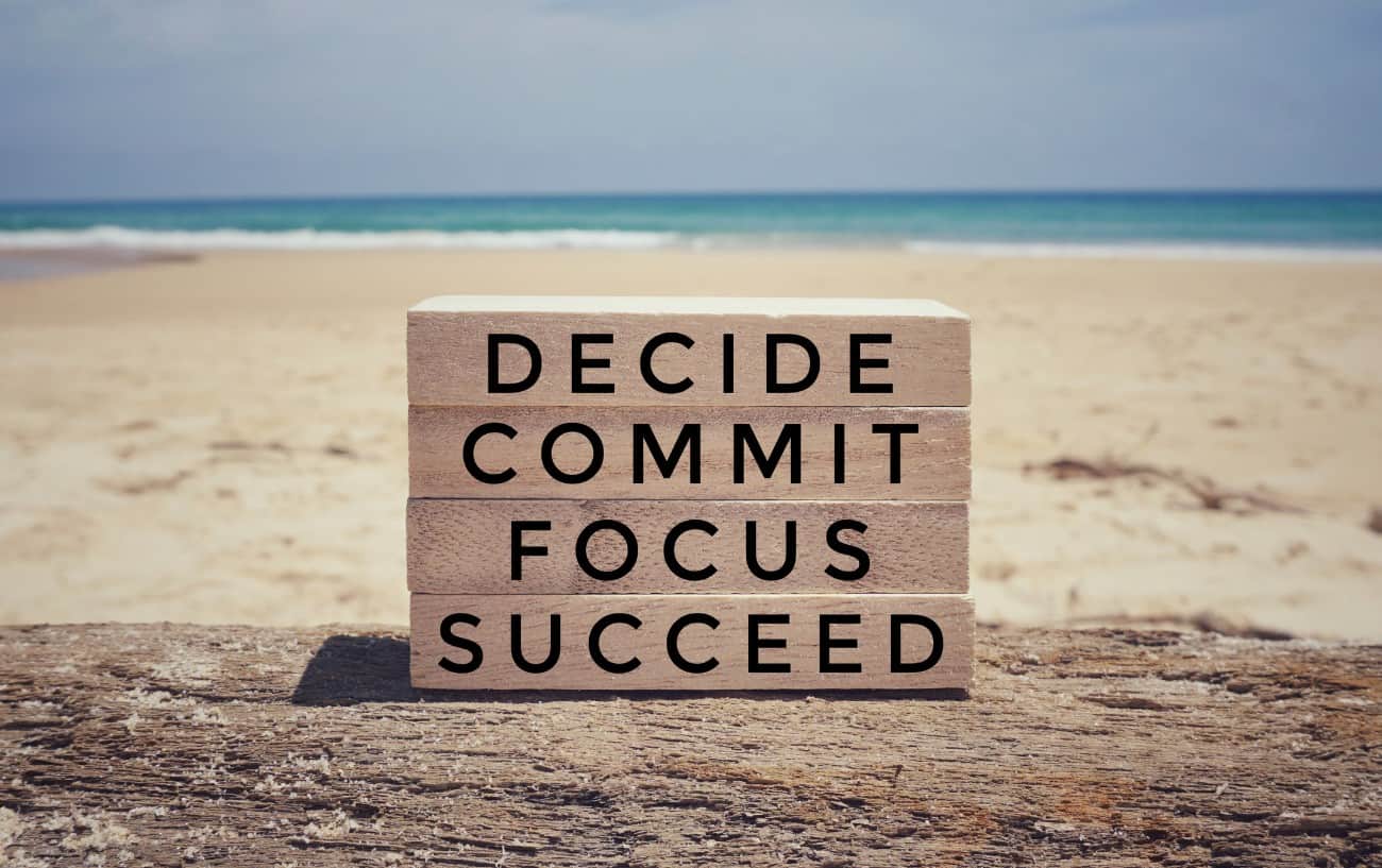 A sign on the beach that says the workout quote: decide, commit, focus, succeed.