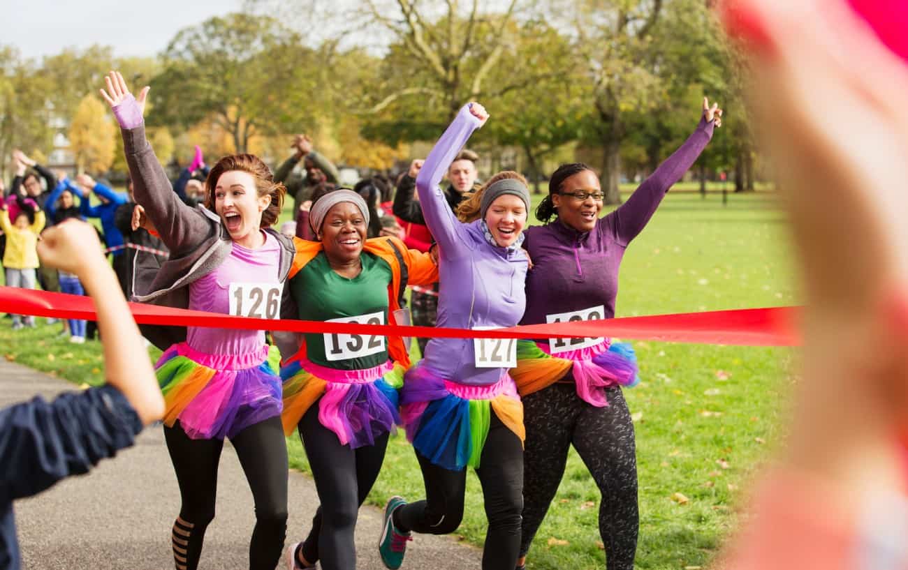 Four people running through a finish line smiling.