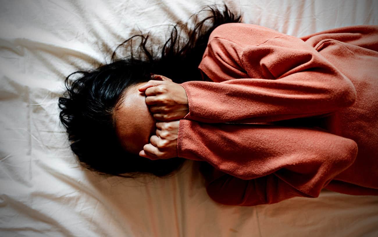 A person lying down in bed with their fists in their face. 