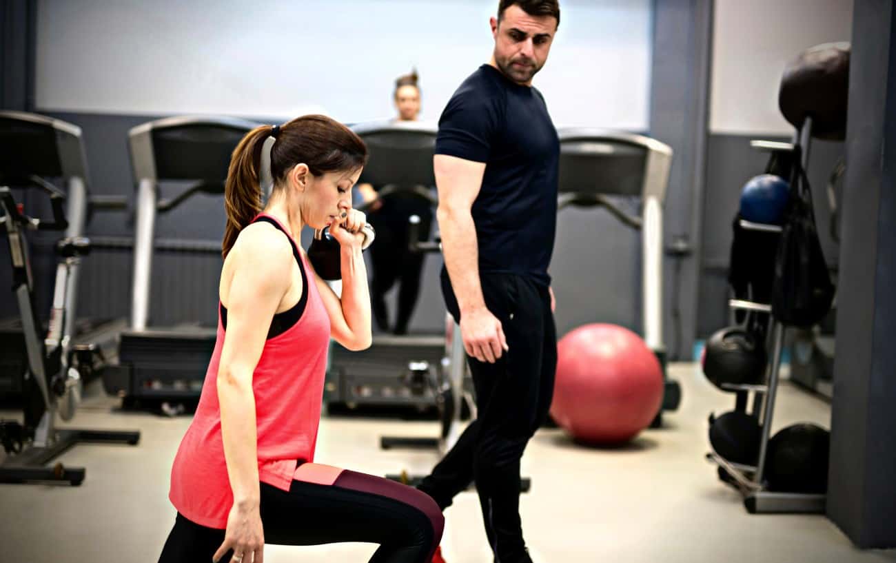 Un entrenador observando a una cliente hacer ejercicio en el gimnasio, enseñándole qué es el entrenamiento de resistencia.