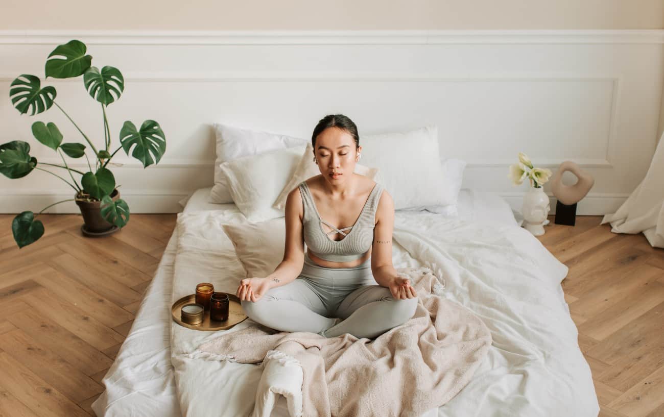 A person meditating on their bed.