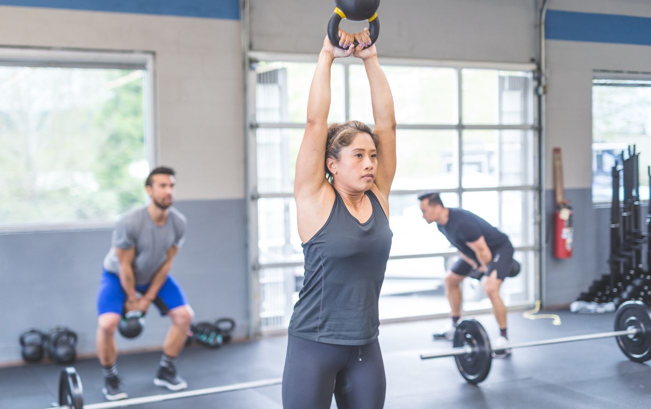 People in a gym with different equipment around, doing kettle bell swings.