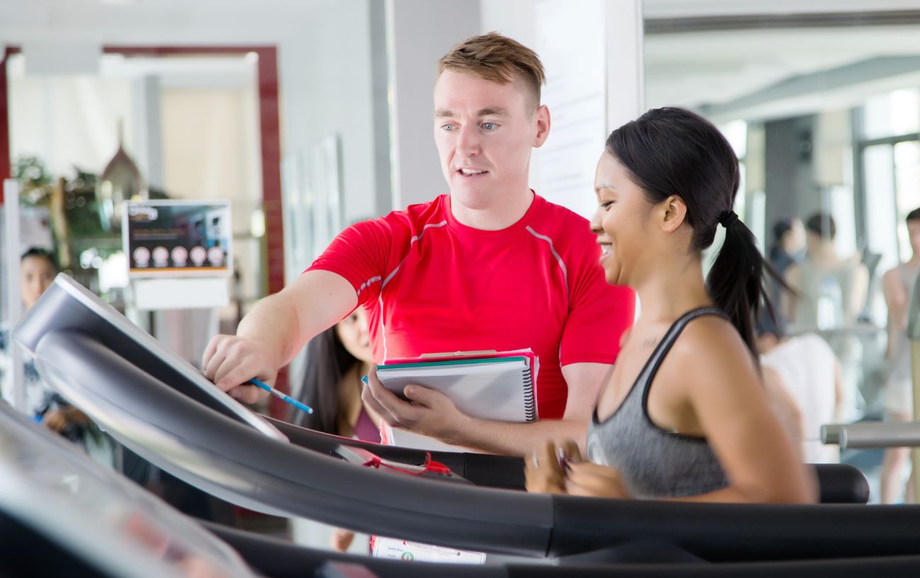 Un entrenador de running en un gimnasio ayudando a un cliente en una caminadora.