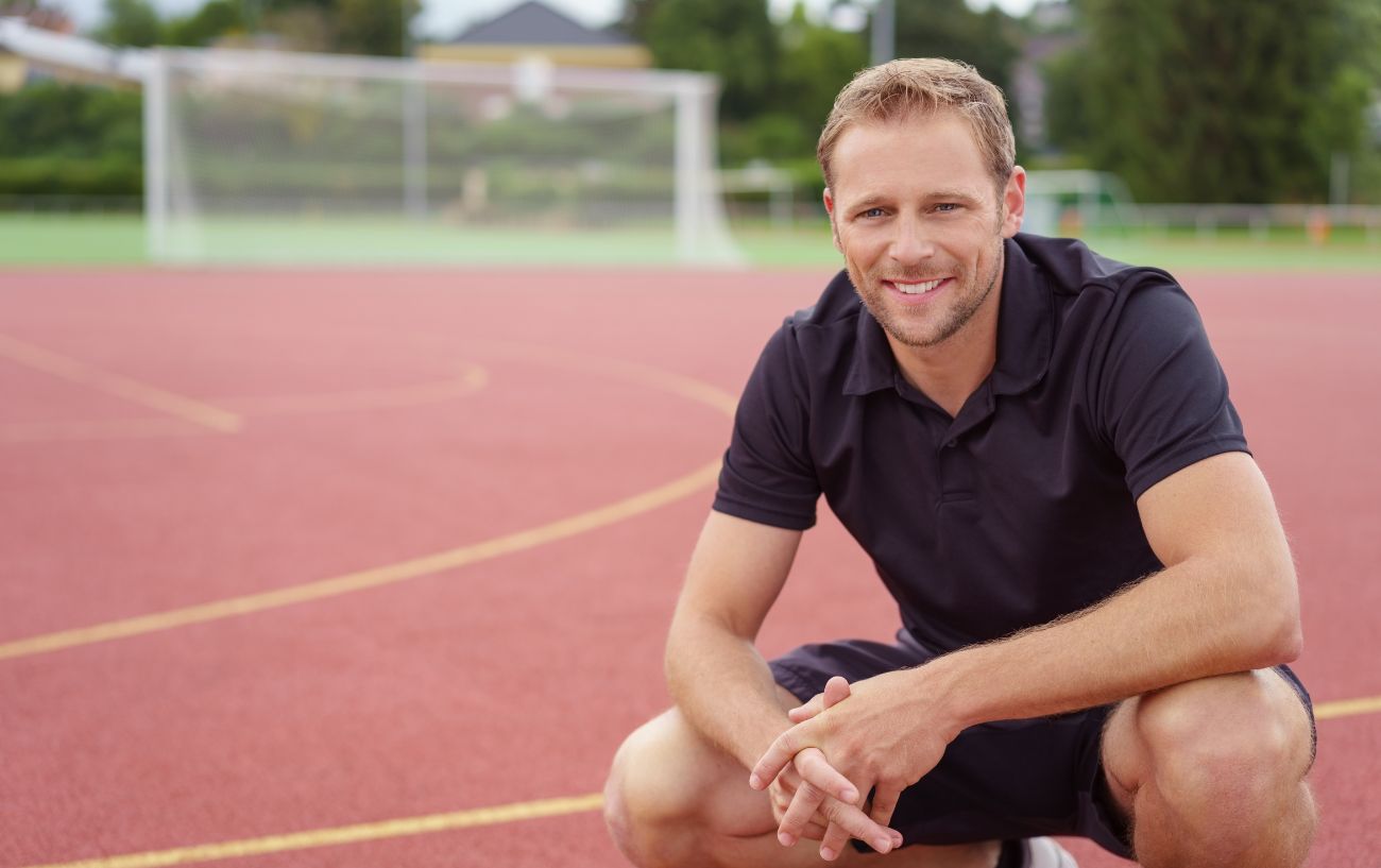 Un entrenador de running arrodillado en una pista.