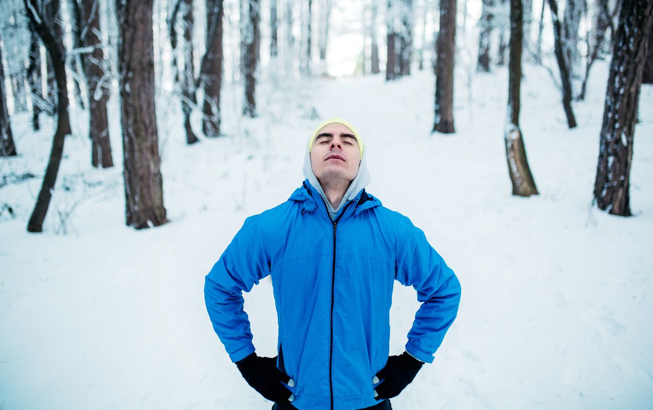 Un corredor detenido en el sendero en la nieve, con los ojos cerrados pensando, ¿por qué es tan difícil correr?