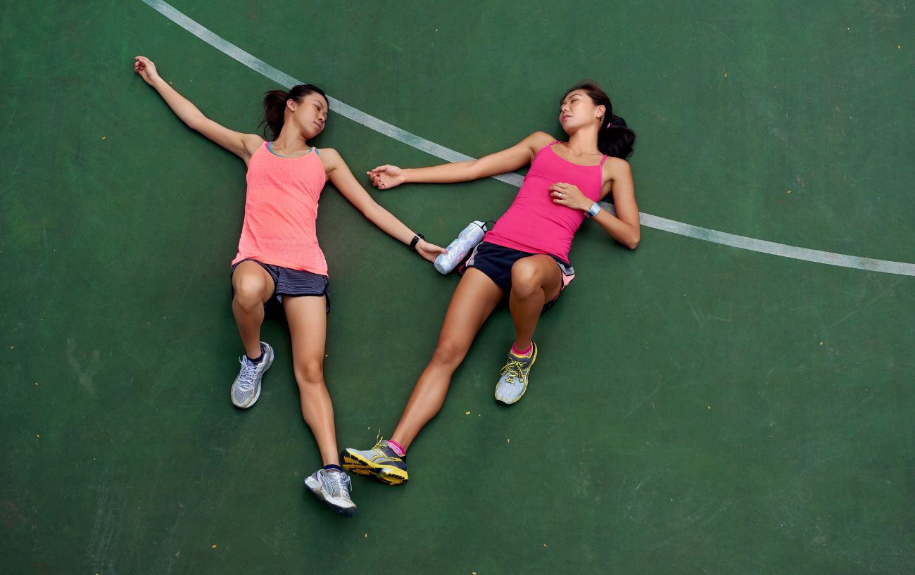 Dos corredores cansados tumbados en una cancha.