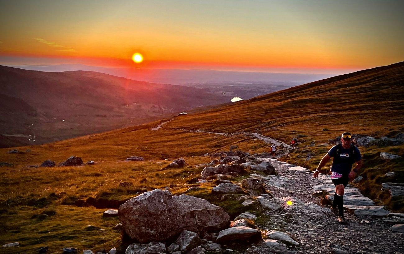 People walking on a rocky trail at sunset.