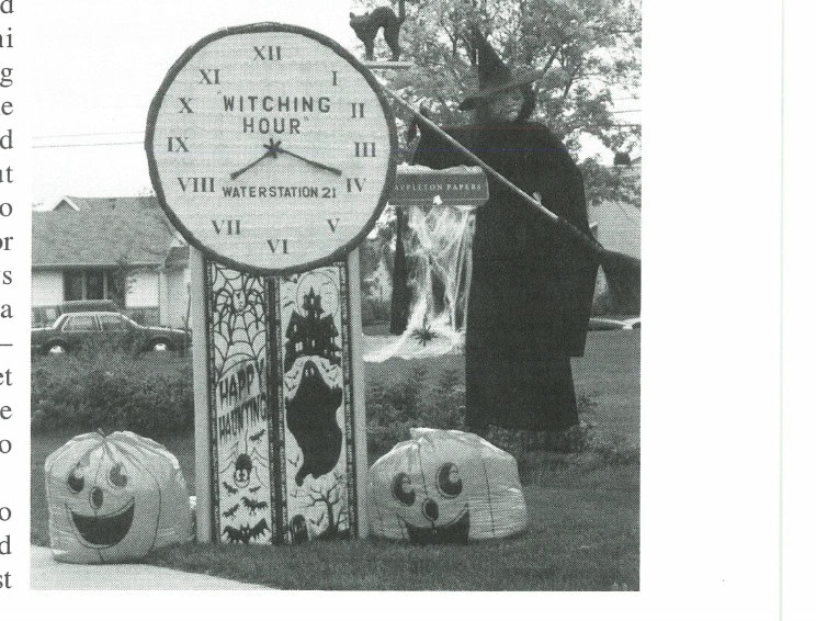 The Appleton Papers water station decorated for Halloween with a witch, a clock reading 'Witching Hour,' and pumpkins. Water Station 21 at the Fox Cities Marathon.