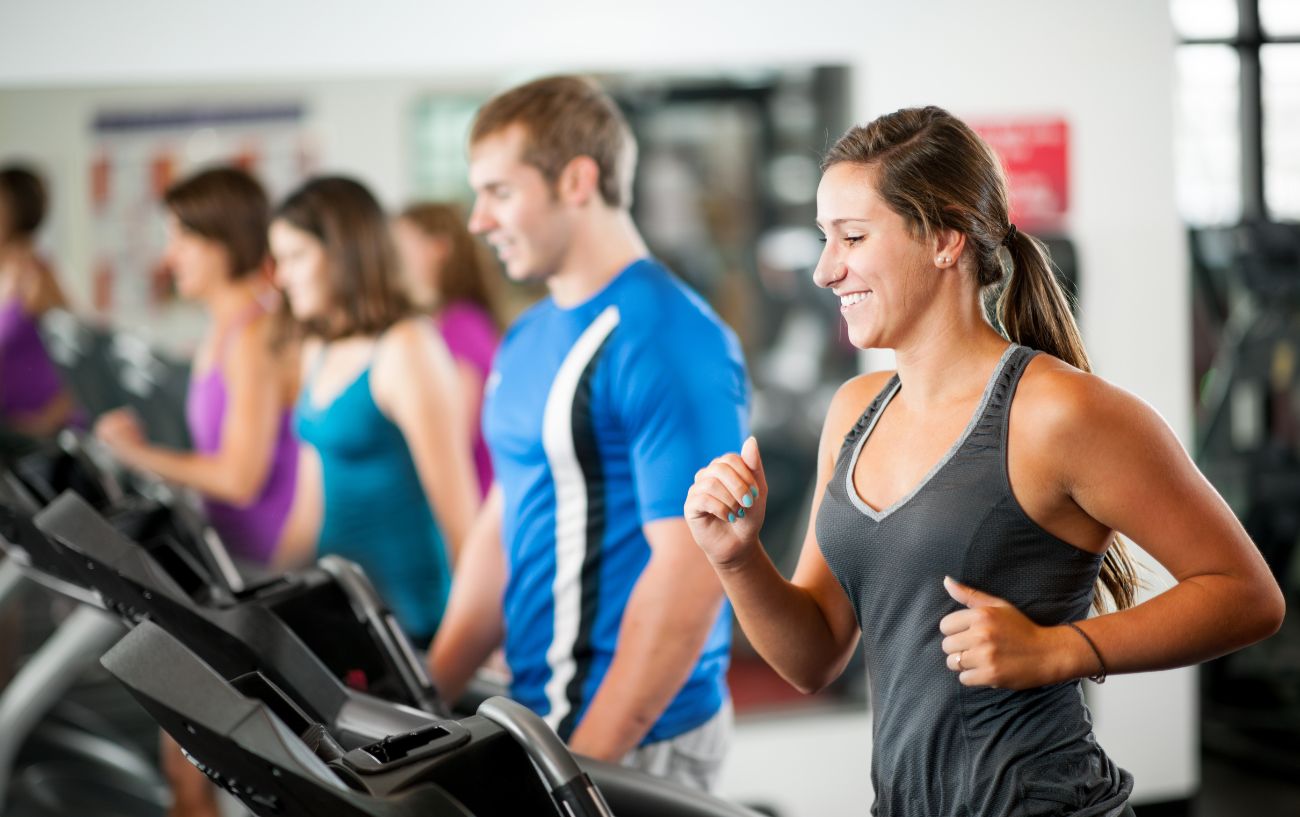 Personas en un gimnasio corriendo y caminando en cintas de correr.