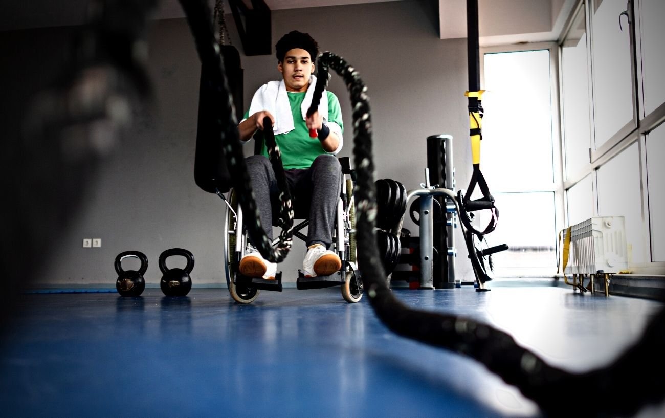 Una persona en silla de ruedas en un gimnasio usando cuerdas de batalla.