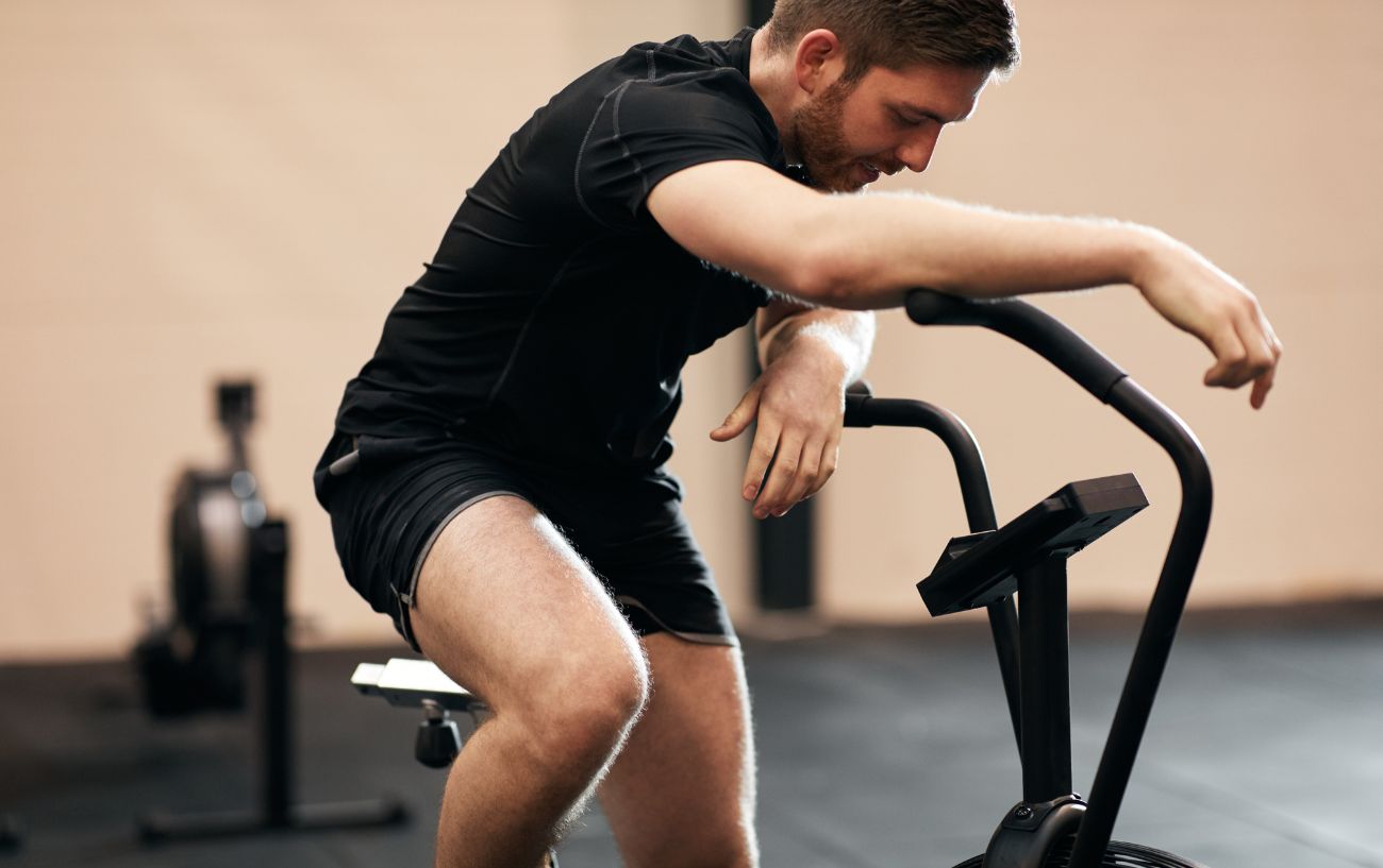 A person leaning over on a stationary bike with a headache from working out.