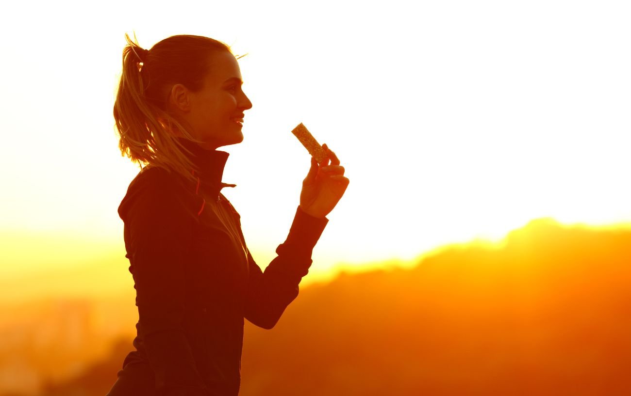 A person eating a granola bar at sunset.