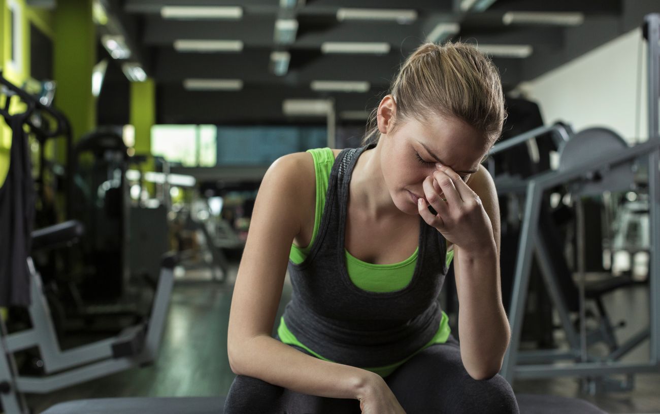 A person sitting on a gym bench with a headache from working out.