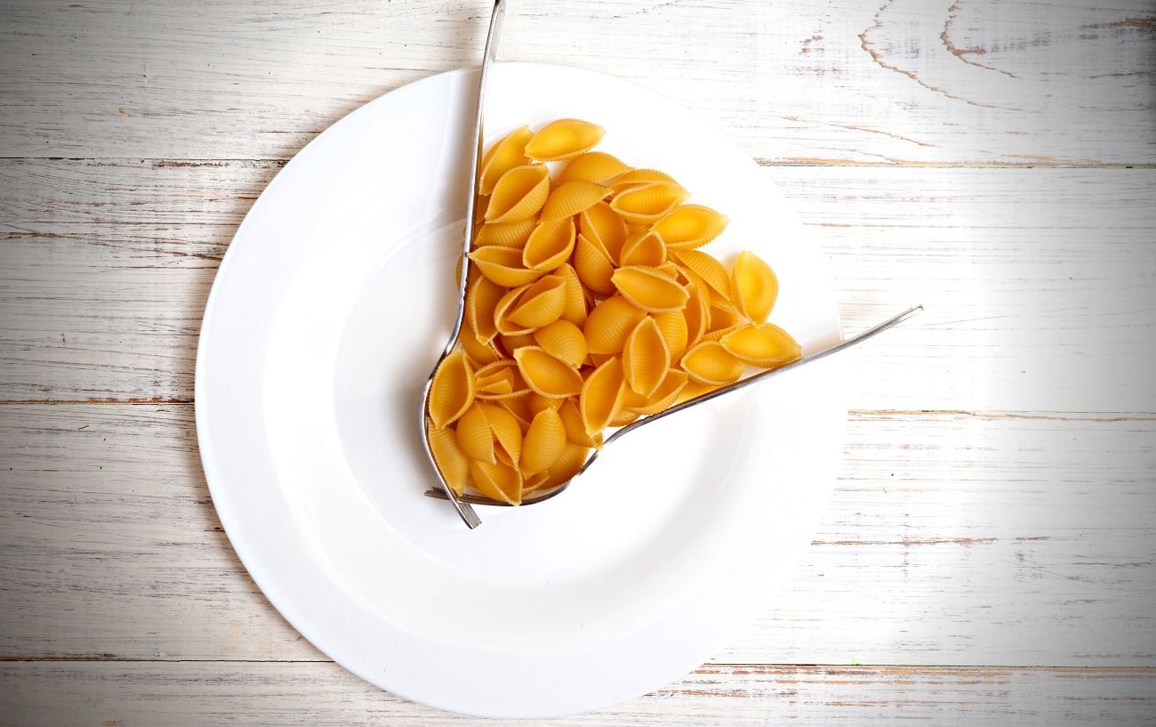 Un plato con pasta y utensilios actuando como manecillas de reloj.