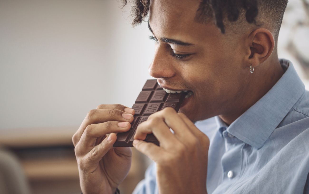 A person taking a bite of a chocolate bar.