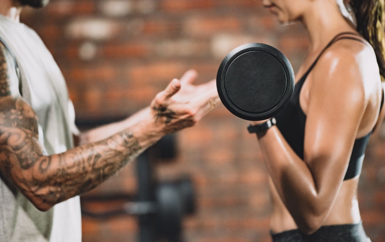 A trainer assisting someone doing a bicep curl, a way of how to build muscle fast.