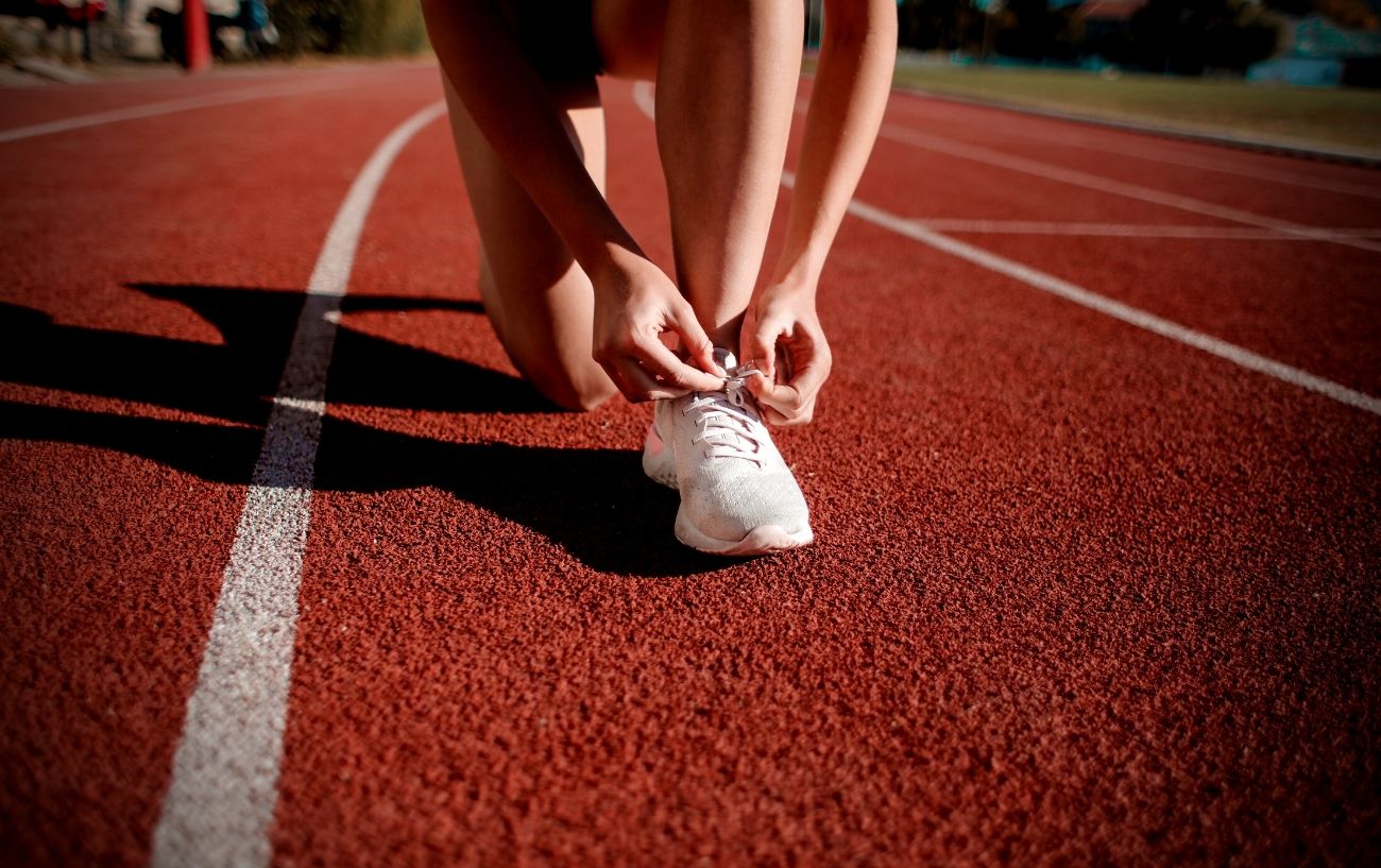 A person lacing up their running shoe on a track.