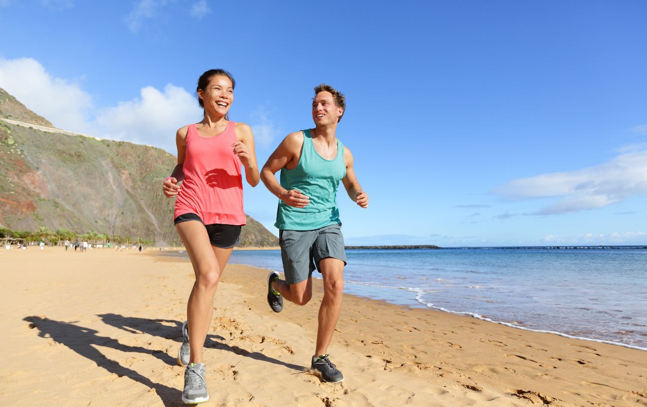 How To Run Longer Without Stopping 7 Two people laughing and running on the beach.