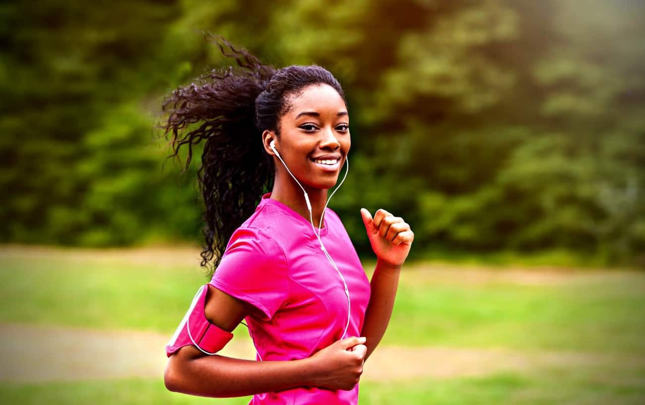 How To Improve Running Form: 29 Ways To Run More Efficiently 1 A woman running listening to music and smiling at the camera.