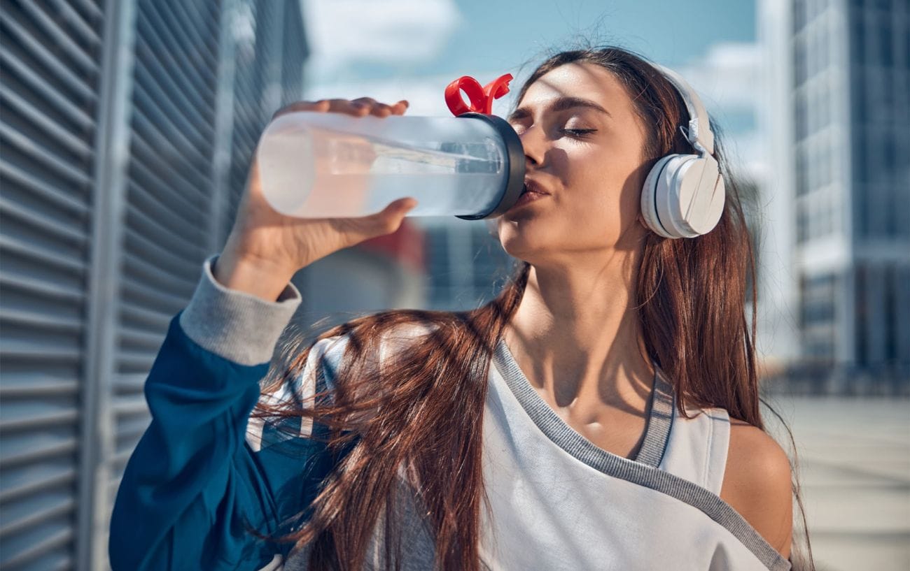 Hydration For Runners: Everything You Need To Know 4 a woman wearing headphones drinking from a bottle