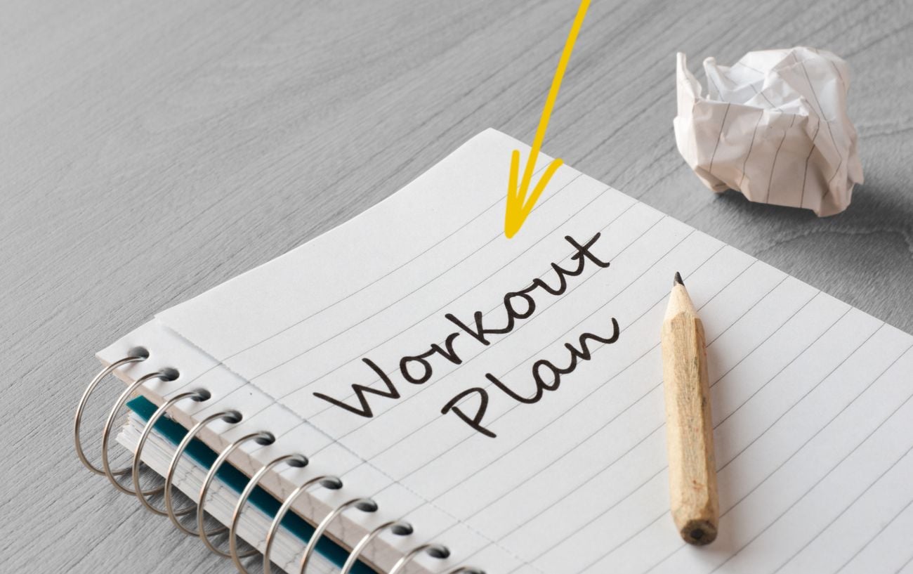 A notebook with the word "workout plan' on it with a pencil.