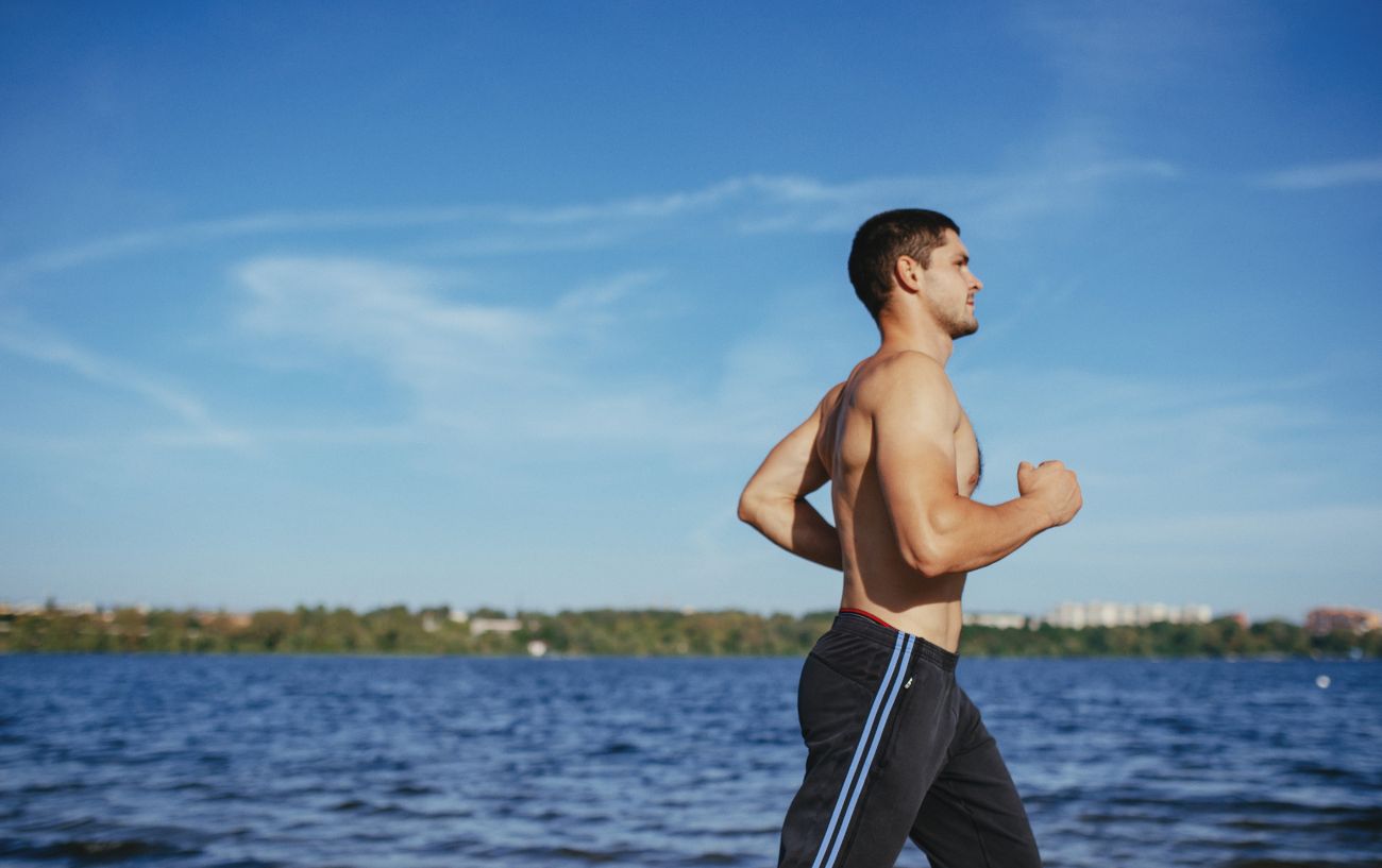 A person jogging on the beach with his shirt off.