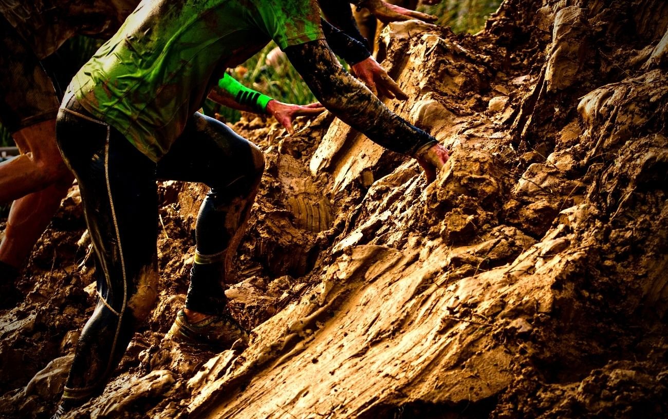 People climbing a muddy wall.