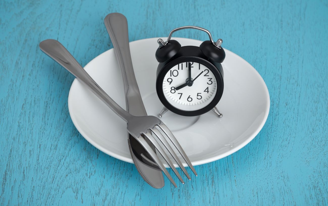 A clock and utensils on an empty plate.