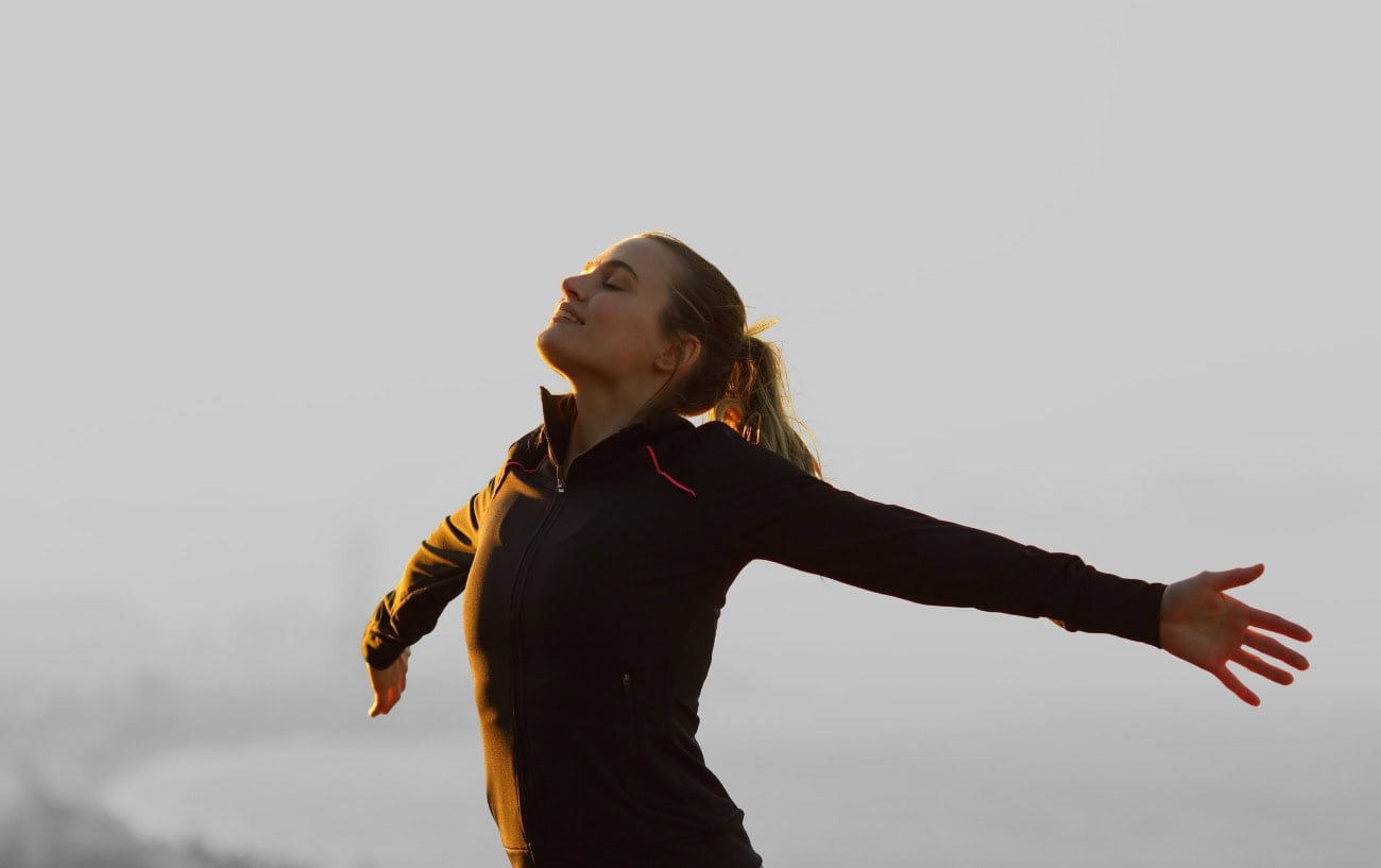 Why Running Feels So Good: The Secret Behind Runner’s Highs and Flow States 1 A woman smiling with open arms.