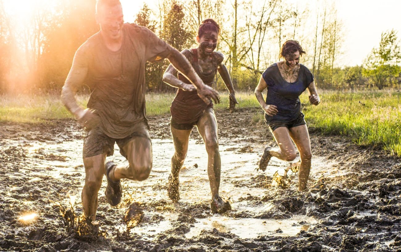 Three people running through the mud in a tough mudder race.