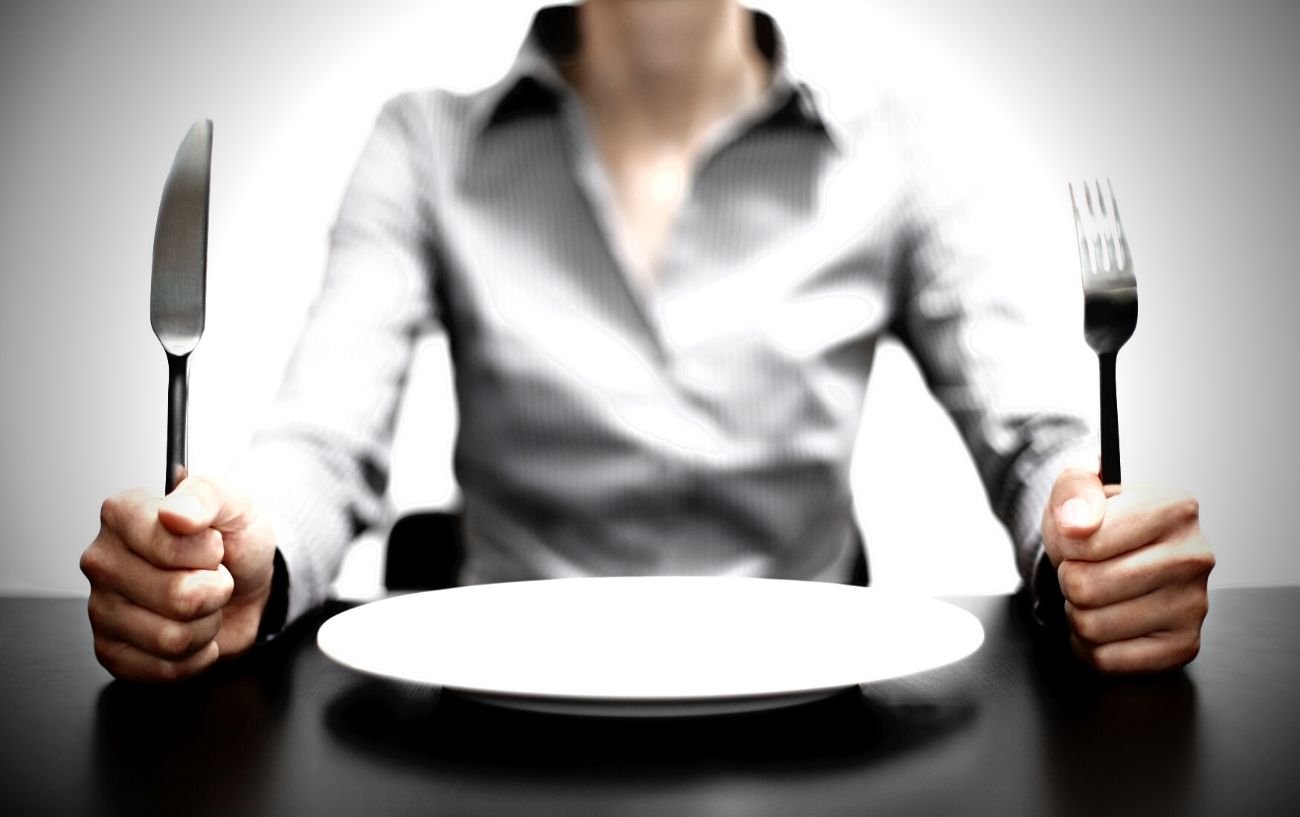 A person who is hungry holding a fork and knife in front of an empty plate.